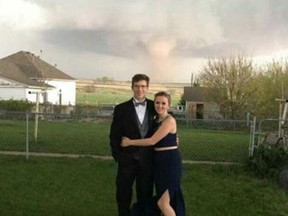 In this Saturday, May 7, 2016, photograph provided courtesy of Heidi Marintzer and taken with a cellphone, Charlie Bator, left, and Ali Jolie Marintzer pose for a photograph before going to prom at the local high school as a tornado skips across the farmland behind the couple near Wray, Colo. A string of tornadoes bedeviled the small farming communities along the Colorado/Nebraska border Saturday as a spring storm swept across the Mid-Plains. (Photo Courtesy of Heidi Marintzer via AP)