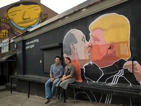 A couple sits in front of graffiti depicting Russian President Vladimir Putin, left, and Republican presidential candidate Donald Trump, on the walls of a restaurant in the old town in Vilnius, Lithuania, Saturday, May 14, 2016. (AP Photo/Mindaugas Kulbis)