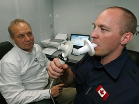 Strathcona County firefighter Jason Biggeman (right) blows into a spirometer to test his lung function after returning from fighting the forest fire near Fort McMurray, Alberta. Professor Jeremy Beach (left, Dept. of Medicine, University of Alberta) was part of a team conducting the tests on the firefighters in Sherwood Park on May 18, 2016. (Larry Wong photo)