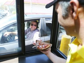 Al Gurhan of the new pizza drive through restaurant named Drive Pie gives a pizza slice to client Peter Friesz . Photo by Jean Levac