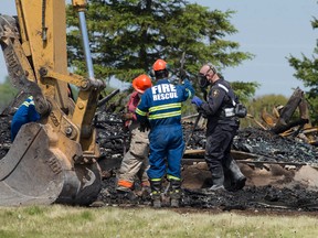 An investigator with the Ontario Fire Marshal's office and members of the Dutton-Dunwich Fire Department sift through the charred remains of a home at 31222 Edinborough Line, where a 37-year-old woman was found dead, near Dutton, Ont. on Sunday (Craig Glover/The London Free Press/Postmedia Network)