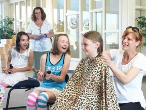 Cathy Burns, standing, community office manager of the Canadian Cancer Society, looks on as Hannah Jefferies, a local hairstylist at Hair by Hannah, cuts the hair of Valley View Public School students Samantha Bisaillon, left, Jasmine Bisaillon and Keyra Smith on Tuesday. Supplied photo