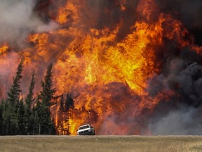 Smoke and flames from the wildfires erupt behind a car on the highway near Fort McMurray, Alta., May 7, 2016. REUTERS/Mark Blinch