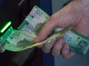 A man inserts Canadian currency into an ATM. (David Ryder/Getty Images)