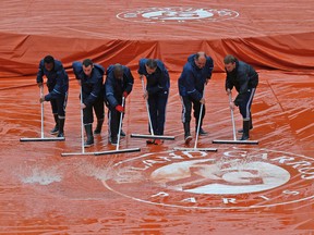 Stadium workers remove water from a protective cover on centre court at the Roland Garros stadium during the French Open in Paris Tuesday, May 31, 2016. (AP Photo/Michel Euler)