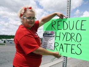 Sharon Chartrand posts a sign on Municipal Road 24 in Lively at a Hydro One - Enough is Enough event to protest high hydro prices. (Ben Leeson/Sudbury Star)