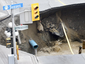 Water splashes as soil collapses into a large sinkhole that formed on Rideau Street next to the Rideau Centre Mall on Wednesday, June 8, 2016 in Ottawa. (Justin Tang, The Canadian Press)