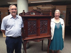St. Thomas Public Library board chairman Greg Grondin and chief librarian Rudi Denham stand with an antique music cabinet from Alma College purchased by the library last summer. The historic piece was from the estate of library benefactor Mary Ann Neely who passed away in January 2015. The Alma antique is being donated to the Elgin County Museum at a special gathering later this month.