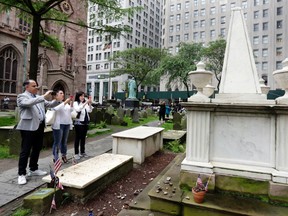 In this June 3, 2016 photo, visitors at the cemetery of Trinity Church photograph the grave of Alexander Hamilton, in New York's Financial District. Interest in historic sites associated with Hamilton has increased thanks to the hit Broadway musical “Hamilton.” (AP Photo/Richard Drew)