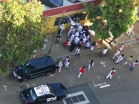 In this Tuesday, June 14, 2016 photo, a crowd of people gather around a wounded person on a sidewalk after gunfire erupted in downtown Oakland, Calif., near a vigil for two drowning victims. Police were searching for suspects Wednesday after the gunfire erupted, leaving at least one girl dead and a few others wounded. (Courtesy of Diana Haven via AP)