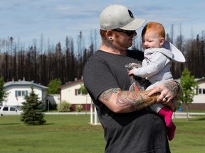 Charred trees are visible in the background as Brandon Gourlay and his seven month-old daughter Zylah Marie Gourlay poses for a photo while taking a walk through the Morgan Heights (Timberlea) neighbourhood, in Fort McMurray on Tuesday June 14, 2016.