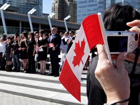 A woman takes a photograph while holding a Canadian flag during a citizenship ceremony in Vancouver, B.C., on July 1, 2009. The Immigration department spent $36,300 on some 330,000 Canadian flags, more than enough for every single immigrant to the country in 2016. (THE CANADIAN PRESS/Darryl Dyck)
