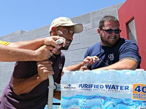 This Tuesday, June 14, 2016 photo Leo Block, left, Matari Phason, center, and Brian Juarez, right, push part of a shipment of 20,000 water bottles donated by Yellow Cab of Phoenix to Central Arizona Shelter Services, Arizona's largest homeless shelter, to help prepare for the summer heat in Phoenix, Ariz. (AP Photo/Ryan Van Velzer)