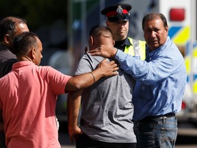 A man is consoled by an Edmonton Police Service officer and bystanders after a male pedestrian was killed in a hit and run at 48 Street and Mill Woods Road South in Edmonton, Alta., on Monday June 20, 2016. A driver was arrested by police a short distance away. IAN KUCERAK/Postmedia News