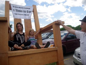 Sonya White, with her daughter Zekeconna White, and Bryan Smith, check out a giant rocking chair brought to Woodstock Tuesday afternoon by the Ontario Health Coalition to raise awareness about the lack of staffing at long-term care facilities. HEATHER RIVERS/WOODSTOCK SENTINEL-REVIEW