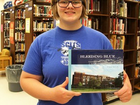 Addie Bicum poses with a copy of her book, Bleeding Blue, in the SCITS library. The book includes quotes from alumni the Grade 11 student interviewed for the self-guided school project. (Tyler Kula/Sarnia Observer/Postmedia Network)