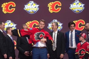 SIXTH PICK: MATTHEW TKACHUK, CALGARY FLAMESMatthew Tkachuk, sixth overall pick, pulls on his sweater as he stands on stage with members of the Calgary Flames management team at the NHL draft in Buffalo, N.Y. on Friday June 24, 2016. 
(THE CANADIAN PRESS/Nathan Denette)