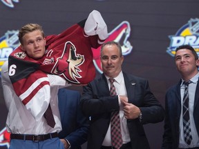 Jakob Chychrun puts on his sweater as he stands on stage with members of the Arizona Coyotes management team at the NHL draft in Buffalo, N.Y. on Friday June 24, 2016. (THE CANADIAN PRESS/Nathan Denette)
