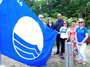 Gathered around the Blue Falg raised Wednesday at Port Glasgow Beach are West Elgin Recreation Superintendent Jeff Slater, left; Wendie Dupuis, owner of Lakewood Trailer Estates who encouraged West Elgin to nominate the beach for a blue flag; Alan Smith general manager, Elgin County Tourism; Isabel Balarezo of Environmental Defence; West Elgin Deputy Mayor Mary Bodnar; and Joanne Wolnik of Ontario Southwest tourism.