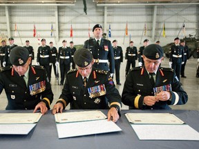 Brig.-Gen. Simon Hetherington (right), new commander of 3rd Canadian Division; Lt.-Gen. Marquis Hainse (centre), chief of the army staff; and Brig.-Gen. Wayne Eyre, outgoing commander of 3rd Canadian Division, sign documents during the change of command signing ceremony at Edmonton Garrison in Edmonton July 11, 2016