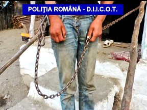 In this Wednesday, July 13, 2016 image taken from a Romanian Police handout video a chained man stands in the doorway of a house in the village of Berevoiesti, Romania. Dozens of vulnerable persons were kidnapped, chained up, whipped, fed scraps of food and forced into manual labor or fighting for entertainment over an eight-year period in rural southern Romania, prosecutors said Wednesday, with police rescuing three men and two boys aged 10-12 found chained up during searches at the homes of the suspects — members of an extended family.(DIICOT-Romanian Police via AP)