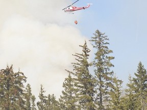 A helicopter prepares to drop water on the flames while helping fight a large wildfire near Duffield in April. The wildfire cost nearly $2 million to fight, and Parkland County wants the province to assist municipalities outside the Forest Protection Area without a fee. - File photo