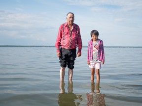 Robert Cardinao and his granddaughter Babe Oseemeemow, who has arthritis, dip their legs in the healing waters of Lac St. Anne during the 2016 Lac St. Anne Pilgrimage in Parkland County on Saturday, July 16, 2016. 
Below, a woman prays before the statue of Saint Anne, located near the shrine of Saint Anne. - Photo by Yasmin Mayne