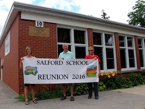 Janis Anstee, left, Larry Bartram and Kathy Geltink, members of the Salford school reunion committee, show off the banner for the August event in front of the former Salford School No. 2, now the local community centre. (MEGAN STACEY/Woodstock Sentinel-Review)