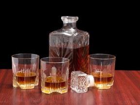 Decanter and three glasses with whiskey, stopper from the decanter on a wooden table on a dark background