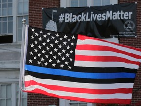 A United States flag, with blue and black stripes in support of law enforcement officers, flies at a protest by police and their supporters outside Somerville City Hall, Thursday, July 28, 2016, in Somerville, Mass. Somerville Mayor Joe Curtatone is promising not to remove a Black Lives Matter banner from City Hall despite complaints from police officers in the state. (AP Photo/Charles Krupa)