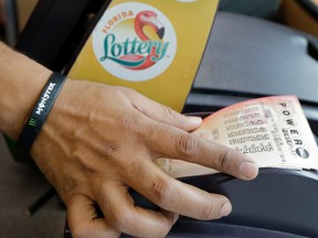 In this Jan. 13, 2016 file photo, a clerk at a convenience store pulls Powerball tickets from a printer for a customer in Tampa, Fla. (AP Photo/Chris O'Meara, File)