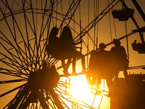 Thrill seekers dangle from the Swing Tower in front of the Ferris wheel  during sunset at The Western Fair in London, Ont. on Monday September 14, 2015. (DEREK RUTTAN, The London Free Press)