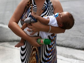 Barbara Betancourt holds her baby Daniel Valdes after being given a can of insect repellent by James Bernat, a City of Miami police officer, as he helps people living around the Miami Rescue Mission prevent mosquito bites that may infect them with the Zika virus on August 2, 2016 in Miami, Florida.  A reported 14 individuals have been infected with the Zika virus by local mosquitoes.  (Photo by Joe Raedle/Getty Images)
