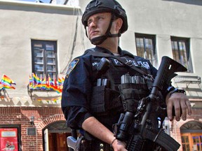 FILE - In this June 12, 2016 file photo, an armed police officer stands guard outside the Stonewall Inn, in New York after a Florida gunman's attack at a gay nightclub spread fear of more attacks. The officer is heavily armed and equipped, in a manner typical of the NYPD's counterterrorism unit and Emergency Service Unit - the NYPD's equivalent of SWAT officers. But the NYPD plans to distribute 20,000 helmets and 6,000 vests before the end of the year to uniformed patrol officers to protect them better during combat with rampaging shooters (AP Photo/Mary Altaffer, File)