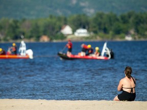 A 10-year-old boy drowned Saturday at Constance Bay. A woman connected to the family sits on the beach watching the first responders search for him.   (Ashley Fraser, Postmedia)