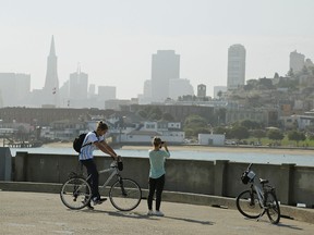 In this Aug. 17, 2015 file photo, a couple on rental bicycles stop to take pictures at Aquatic Park of the hazy skyline in San Francisco. A 20-year-old man was shot to death while playing "Pokemon Go" at a tourist attraction along San Francisco's waterfront, authorities and a family friend said on Sunday. Calvin Riley was shot Saturday night, Aug. 6, 2016, by an unknown assailant at Aquatic Park near Ghiradelli Square, the U.S. Park Police said. (AP Photo/Eric Risberg, File)