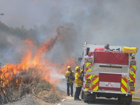 Mike Callaway, of the San Bernardino County Fire Department, attacks burning brush along Highway 173 while battling a wildfire in Hesperia, Calif., Monday, Aug. 8, 2016. (James Quigg/The Daily Press via AP)