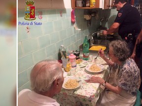 In this recent photo made available by the Italian Police, two police officers serve pasta, after cooking it, to two elderly, after they were called in a Rome neighborhood to check on a couple loudly quarreling on a recent, hot summer night. Police say that four officers who came to the couple's apartment used butter, cheese, spaghetti and "all their humanity" to cook them dinner and ease their loneliness.  (Italian Police Photo via AP)