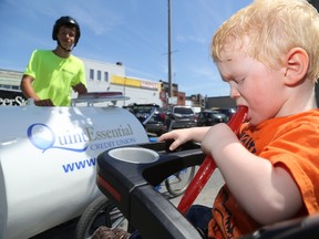 Luke Hendry/The Intelligencer 
Owen Hawkes, 2, bites into an ice pop received for free from Zach Uens, left, in downtown Belleville Tuesday. Uens, hired by QuintEssential Credit Union and sponsored by car dealer Peter Smith, has been touring the city to hand out free water and frozen treats. The city is in the midst of yet another heat wave.