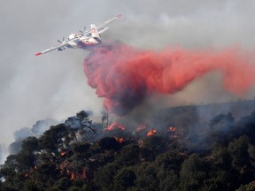 A plane sprays fire extinguisher as part of an attempt to struggle against a fire which has already devastated some 200 hectares in Vitrolles, southern France on August 10, 2016. (AFP PHOTO/BORIS HORVATBORIS)