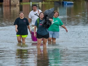 People wade in water near flood damaged homes in Highland Ridge Subdivision in Youngsville, La., Sunday, Aug. 14, 2016. Torrential rains swamped parts of southern Louisiana, causing widespread flooding. (Scott Clause/The Daily Advertiser via AP)