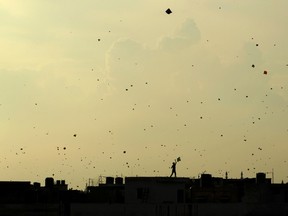 In this Aug. 15, 2013 file photo, a boy flies a kite from the roof of a house as other kites seem to flock in the sky above as Indians celebrate Independence Day in New Delhi, India. Indian police say three people, including two children, have died after their throats were slashed by glass-coated kite string used in competitions to slice the strings of other kites.The deaths occurred in New Delhi on Monday, which was a holiday on account of India's Independence Day when people fly kites to celebrate. (AP Photo/Tsering Topgyal, File)