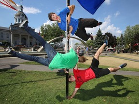 Zach McIver, 19, top, Liam Wilkins, 19, centre, and Curtis Shorts, 16, lift themselves into horizontal positions on a flagpole in Confederation Park on Aug. 12. (Elliot Ferguson/The Whig-Standard)