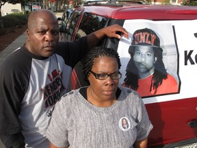 In this Dec. 13, 2013 file photo, Kenneth and Jacquelyn Johnson stand next to a banner on their SUV showing their late son, Kendrick Johnson in Valdosta, Ga. The parents of Kendrick Johnson, who was found dead inside a rolled-up gym mat at school, have dropped a wrongful death lawsuit accusing two brothers of killing their son.  (AP Photo/Russ Bynum, File)