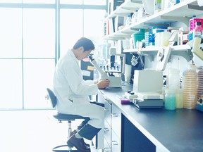 Scientist looking into microscope in research lab, side view (Getty Images)