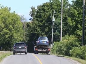 An OPP vehicle escorts a flatbed tow truck as it removes a vehicle from a farmer's field on Holmes Road near Inverary, north of Kingston, on Monday, where the bodies of two people were discovered Sunday evening . (Elliot Ferguson/The Whig-Standard)