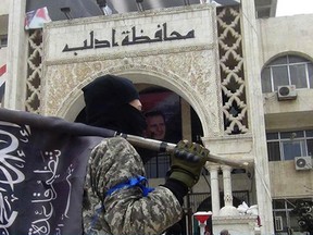 In this file photo posted on the Twitter page of Syria's al-Qaida-linked Al Nusra Front March 28, 2015, which is consistent with AP reporting, a fighter from Syria's al-Qaida-linked Al Nusra Front holds his group flag in front of an Idlib governorate building in Idlib province, north Syria. (Al Nusra Front Twitter page via AP, File)