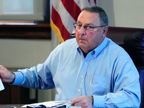Maine Gov. Paul LePage holds up news release with a booking mug shot from a three-ring binder of news releases and articles about drug arrests during a meeting with reporters on Friday, Aug. 26, 2016, in the State House Cabinet room in Augusta, Maine. (Joe Phelan  /The Kennebec Journal via AP)