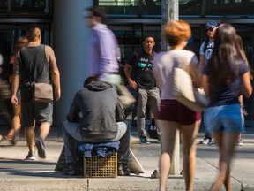 People walk past a man with signs appealing for change or food in downtown Toronto August 23, 2016. (Ernest Doroszuk/Toronto Sun)