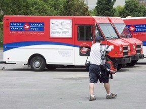 A postal worker walks past Canada Post trucks at a sorting centre in Montreal on July 8, 2016. The Canadian Union of Postal Workers says its plan to begin a rolling overtime ban at midnight Sunday has been placed on hold for 24 hours.CUPW issued a statement late Sunday night that it was delaying any possible job action in a "last ditch effort" to reach a negotiated settlement with Canada Post. (THE CANADIAN PRESS/Ryan Remiorz)